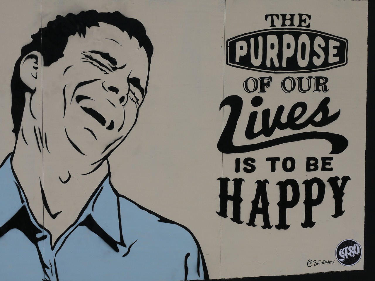 Grafite na parede de homem sorrindo com a frase "O propósito de nossas vidas é ser feliz" 