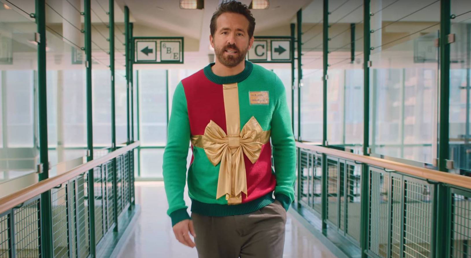 Man walking in a corridor wearing a festive holiday sweater with a large bow