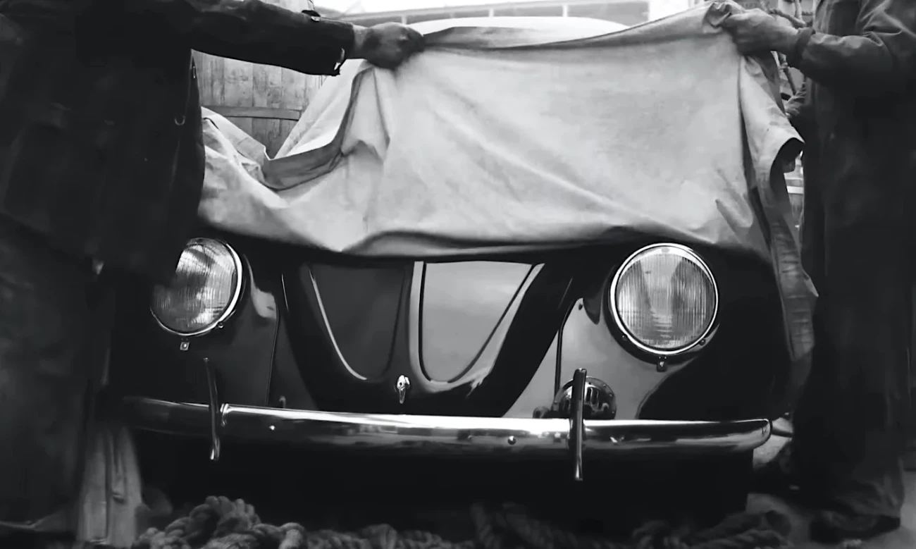Unveiling a vintage car, black and white photo of hands pulling off a cover from classic vehicle headlights and grille