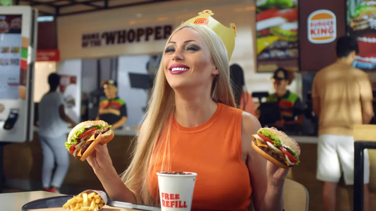 Woman enjoying burgers at Burger King with paper crown and free refill soda cup in a fast-food restaurant setting.