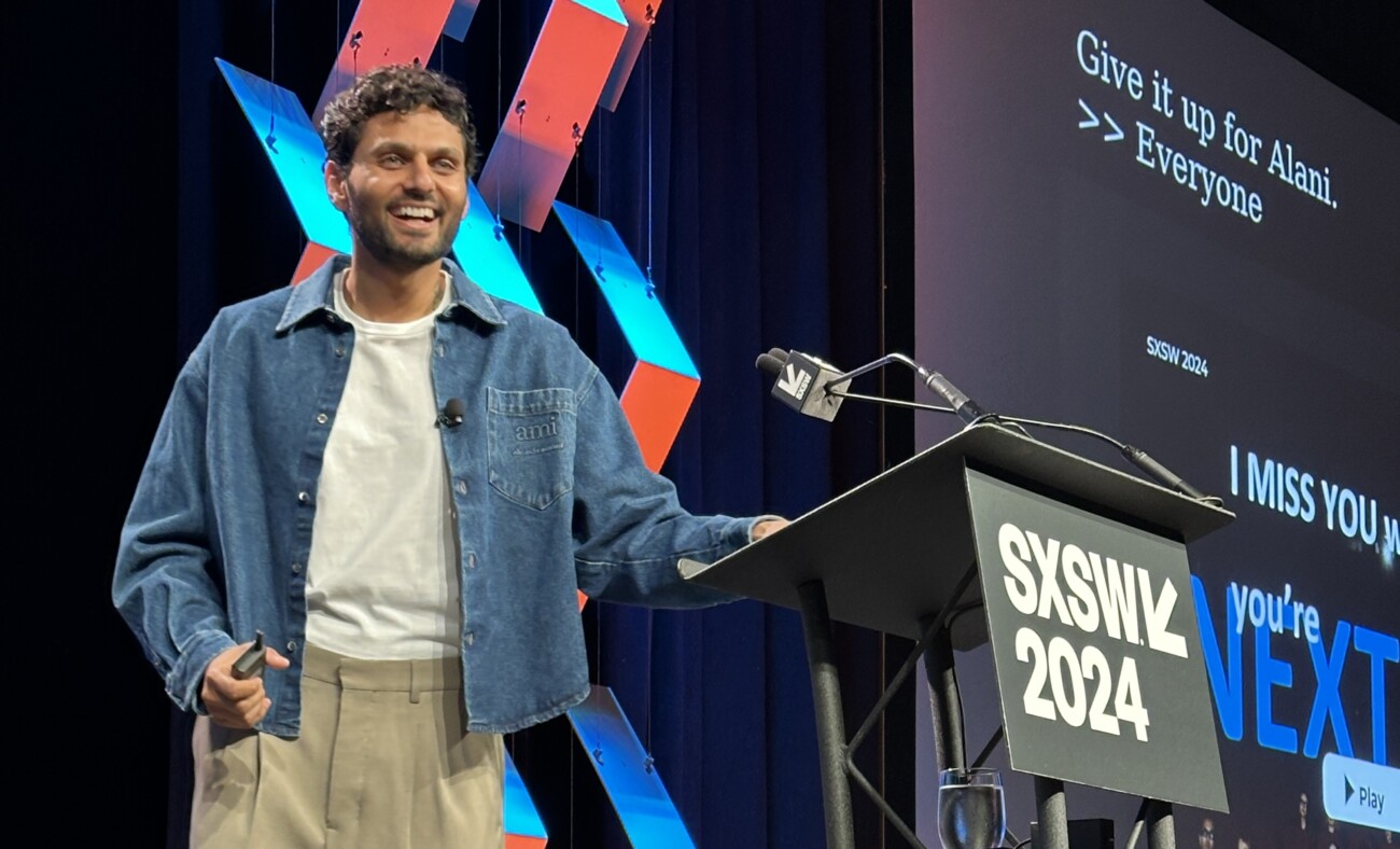 Smiling man standing at podium during SXSW 2024 event with background screen displaying text "Give it up for Alani. >> Everyone"