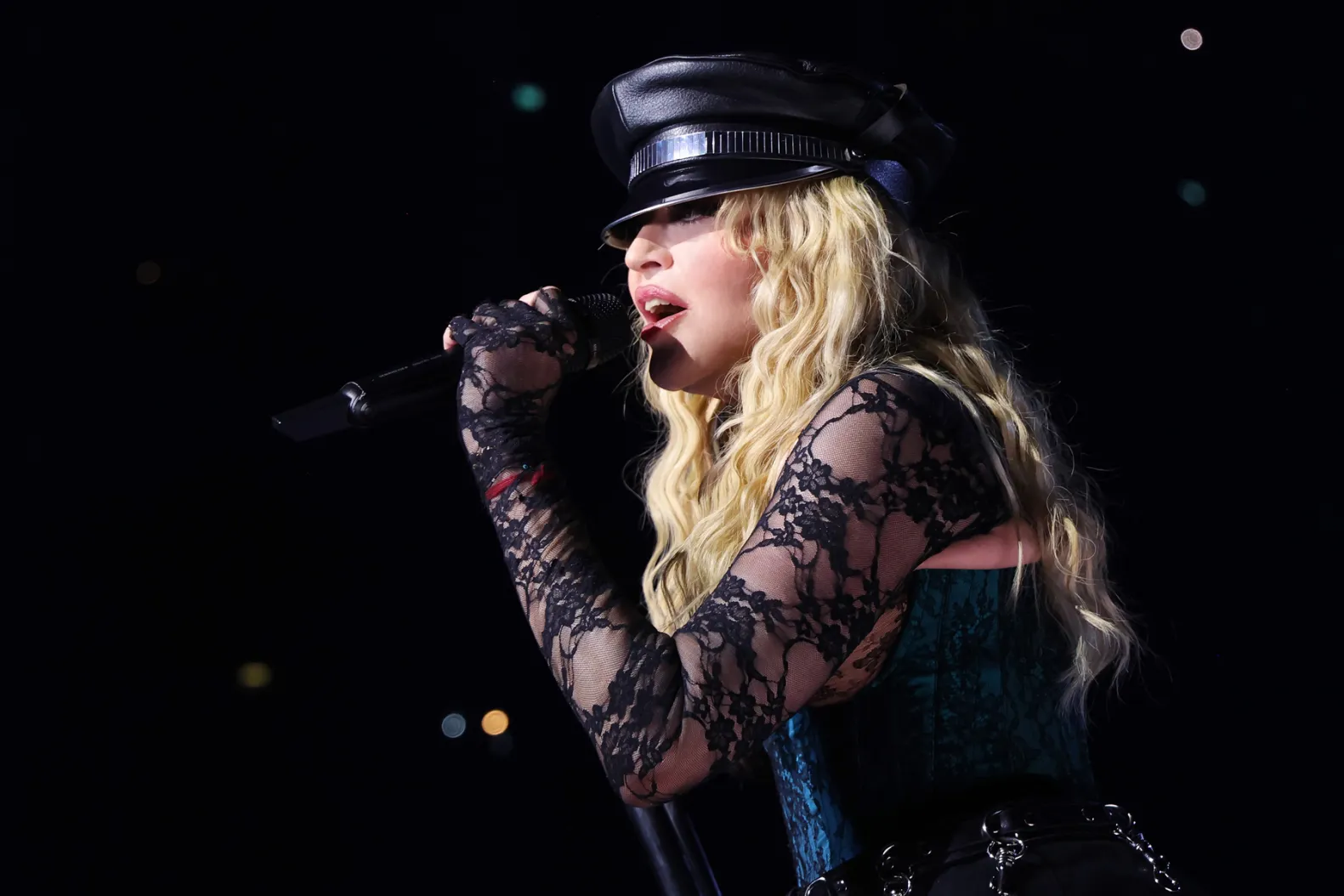Female singer performing on stage with microphone in black lace outfit and leather hat.