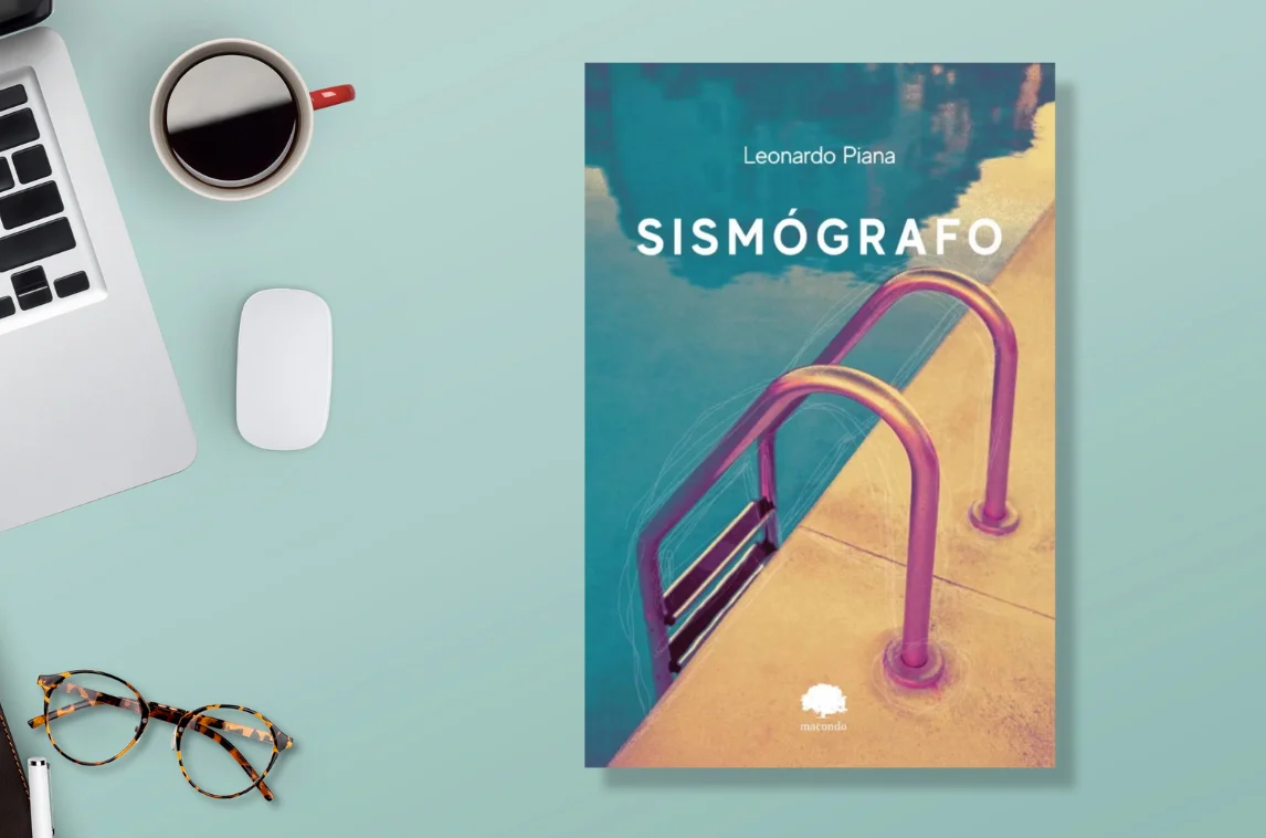 Top view of a workspace with a book titled "Sismógrafo" by Leonardo Piana, alongside a laptop, coffee cup, glasses, and mouse on a teal background.