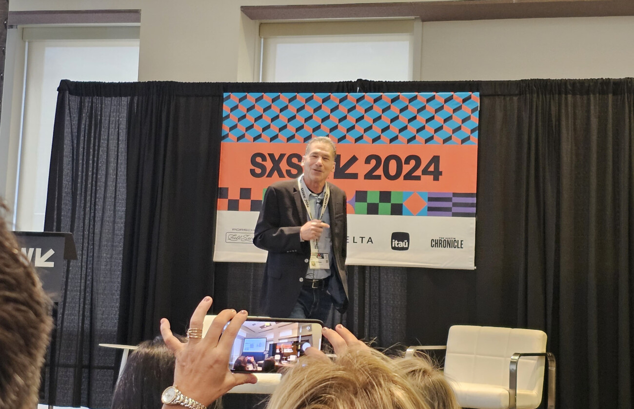 Man presenting at SXSW 2024 event with audience member capturing photo on smartphone.