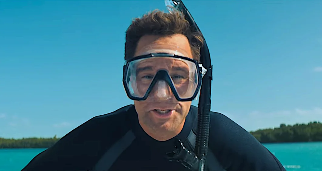 Man wearing diving gear with a snorkel and mask ready for underwater exploration with tropical blue water in the background