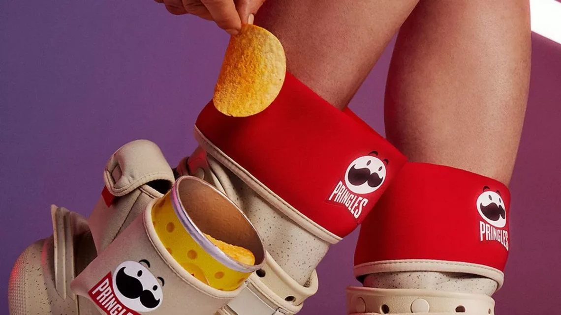 Person wearing crocs with red Pringles-designed shoe charms, pulling a chip from a Pringles can.