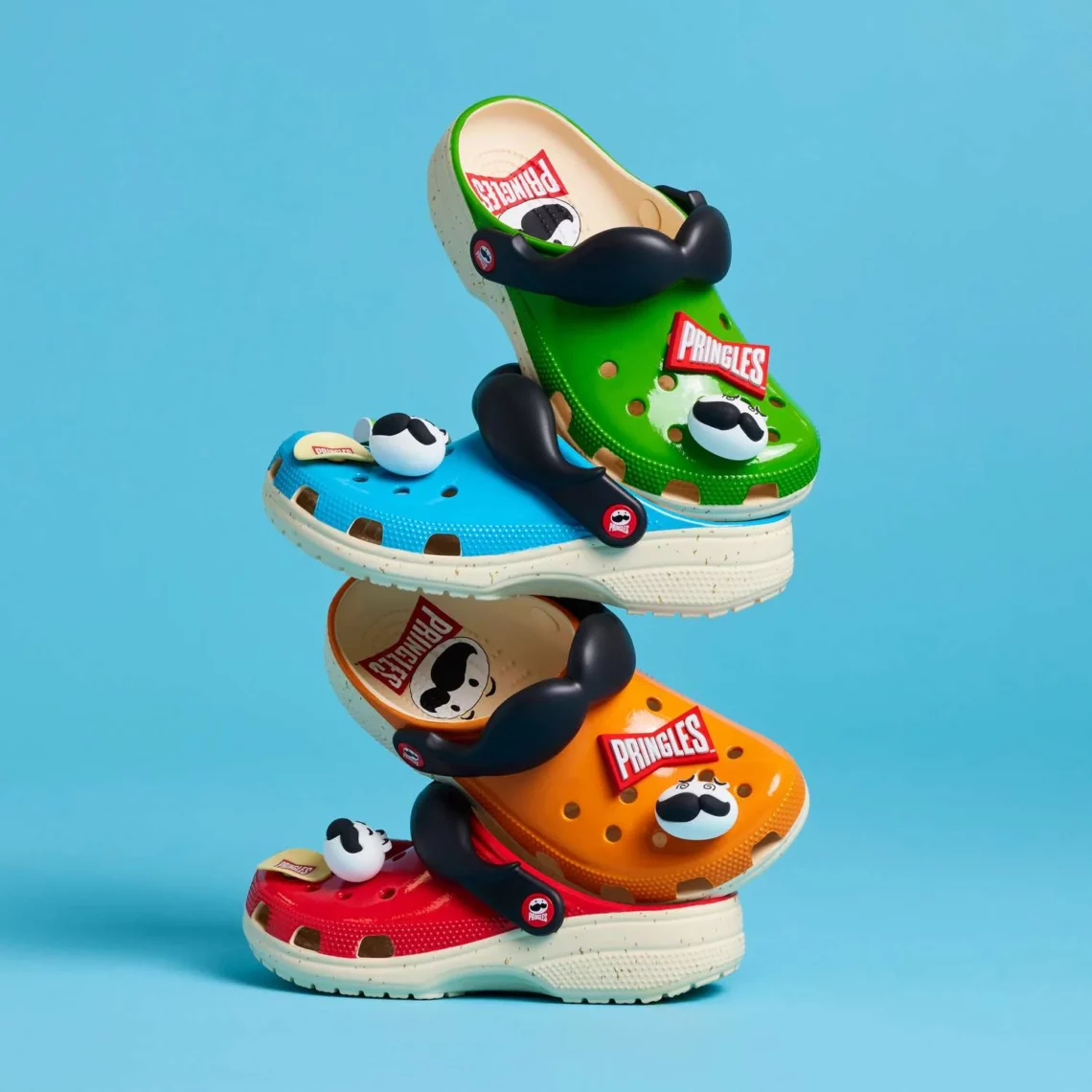 Colorful Pringles branded crocs adorned with mustache and cow print charms on a blue background.