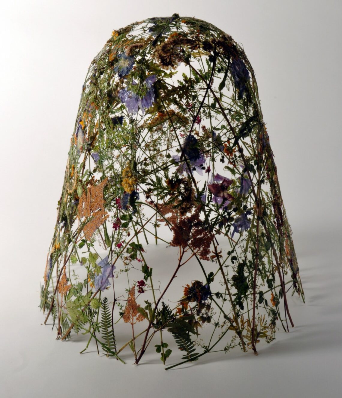 Floral art installation with assorted wildflowers and foliage on a wireframe dome on a white background.