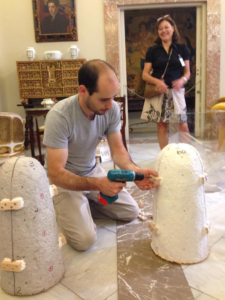 Art conservator restoring sculptures with a handheld drill in a museum while a female observer watches.