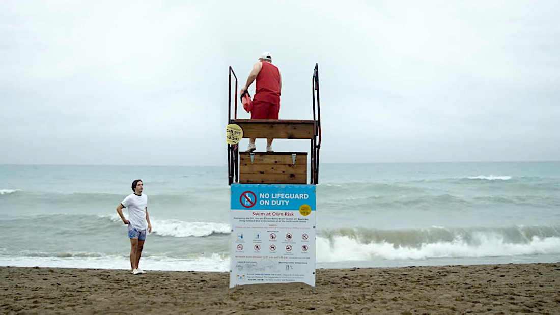 Lifeguard on watchtower overlooking wavy ocean with no lifeguard on duty sign at cloudy beach