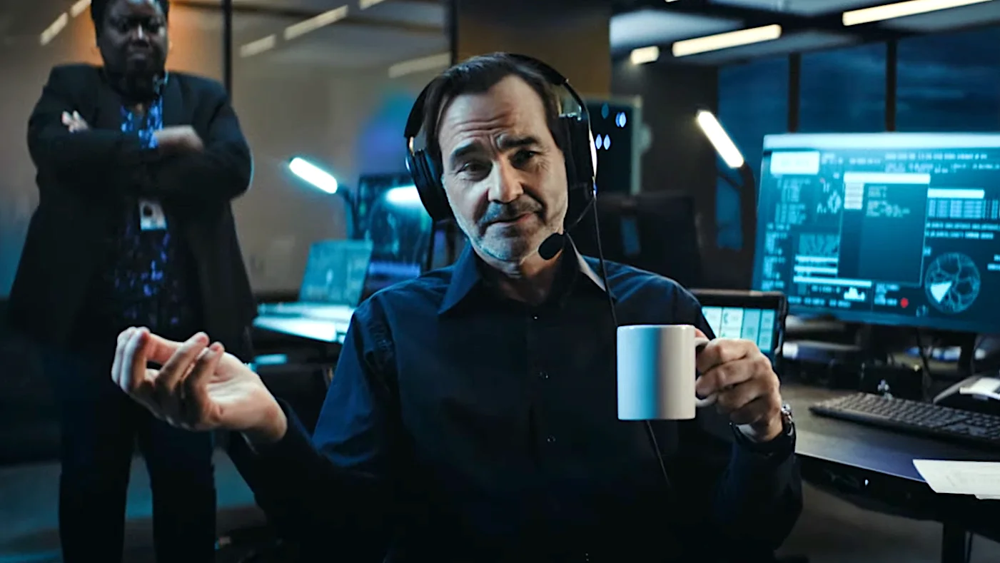 CANAL+ SUPER. Man with headset in a control room holding a mug with colleague standing in the background.