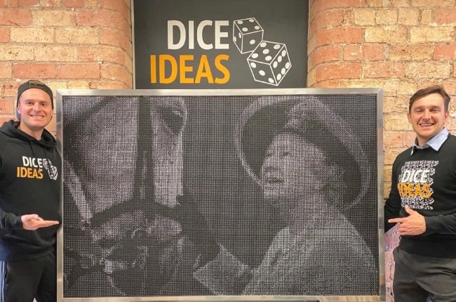 Two men presenting a large dot-style mural at DICE IDEAS office.