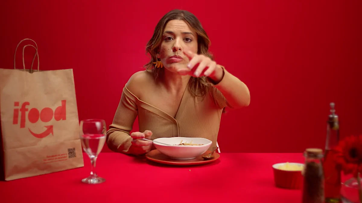 Woman enjoying a meal from iFood delivery service with a red background.