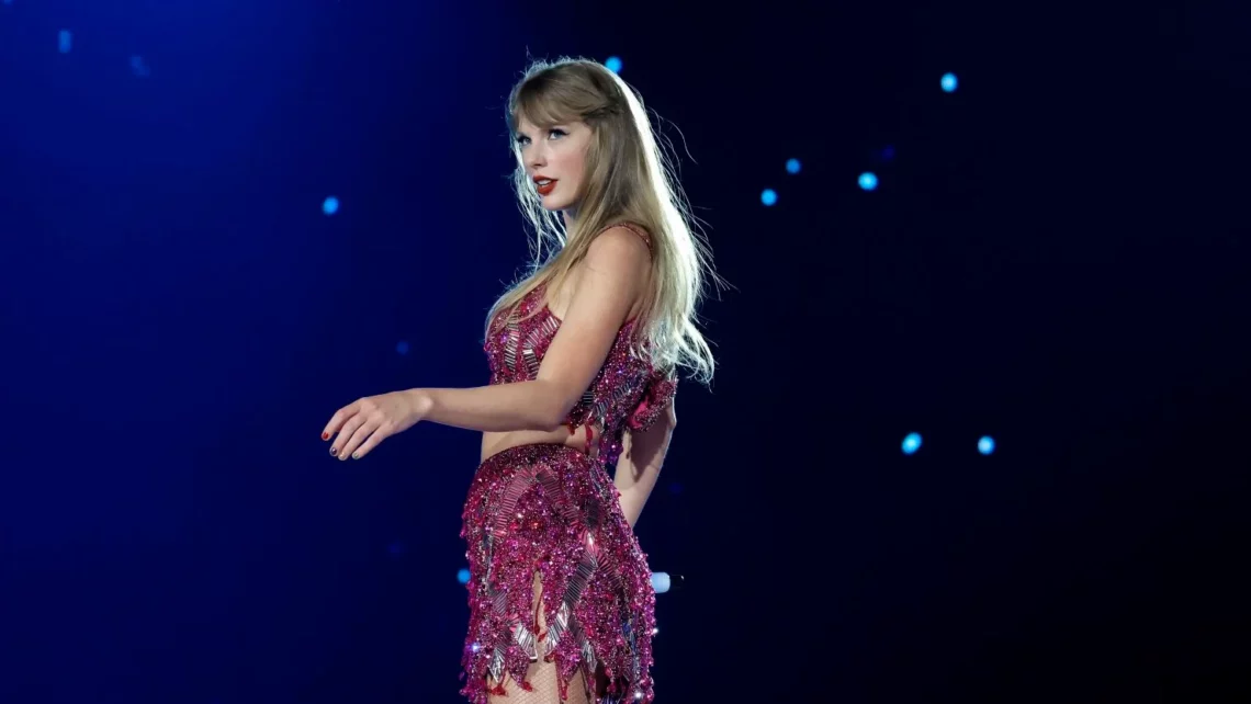 Taylor Swift no TikTok. Female pop singer performing on stage in a sequined red dress against a dark blue background with stage lights.