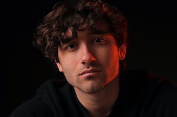 Young man with curly hair in low-key lighting against a dark background