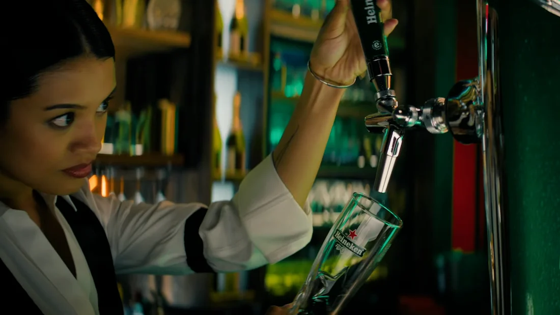 Bartender pouring beer from tap into Heineken glass at bar.
