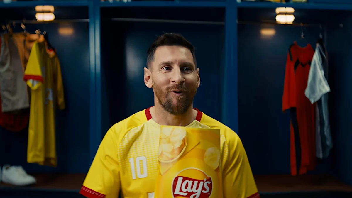 Soccer player in number 10 yellow jersey featuring Lay's logo in a locker room setting with sports gear in the background.
