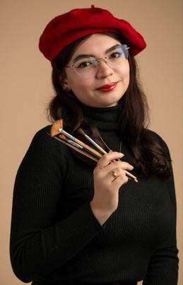 Woman with glasses wearing red beret and black turtleneck holding paintbrushes