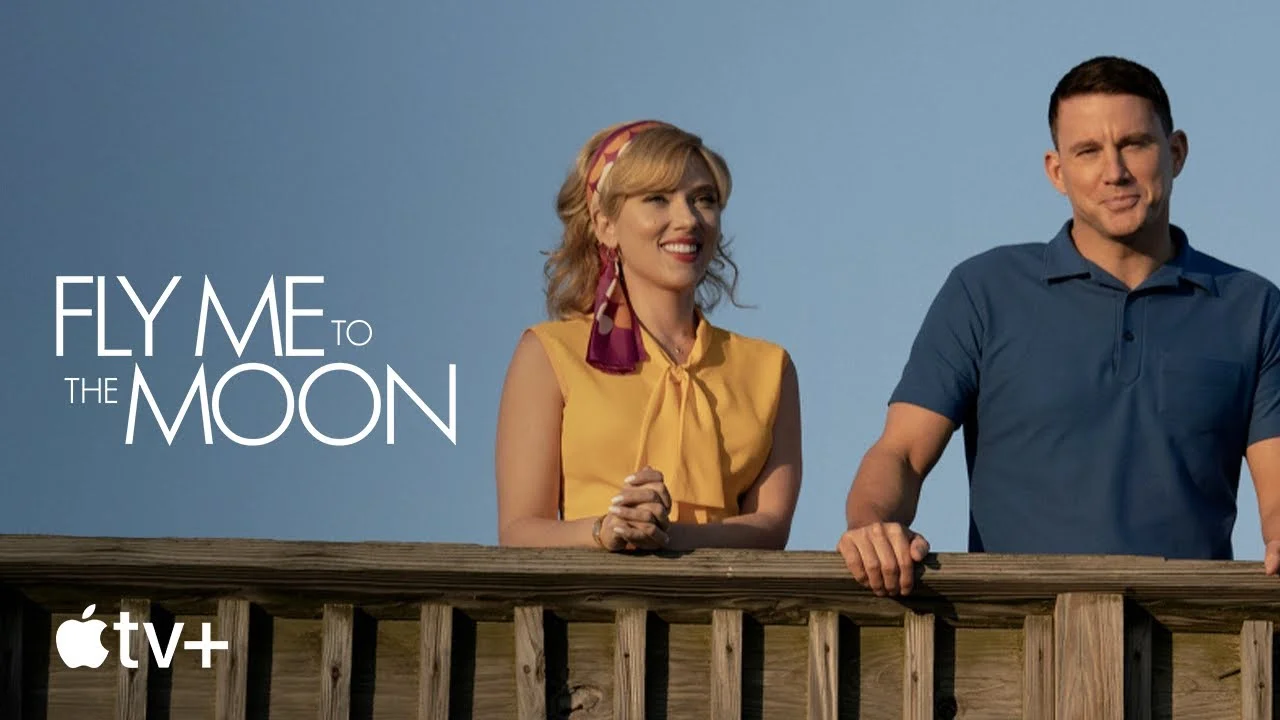 Promotional still from the TV show "Fly Me to the Moon" with two smiling actors leaning on a wooden railing, displayed on Apple TV+ platform.
