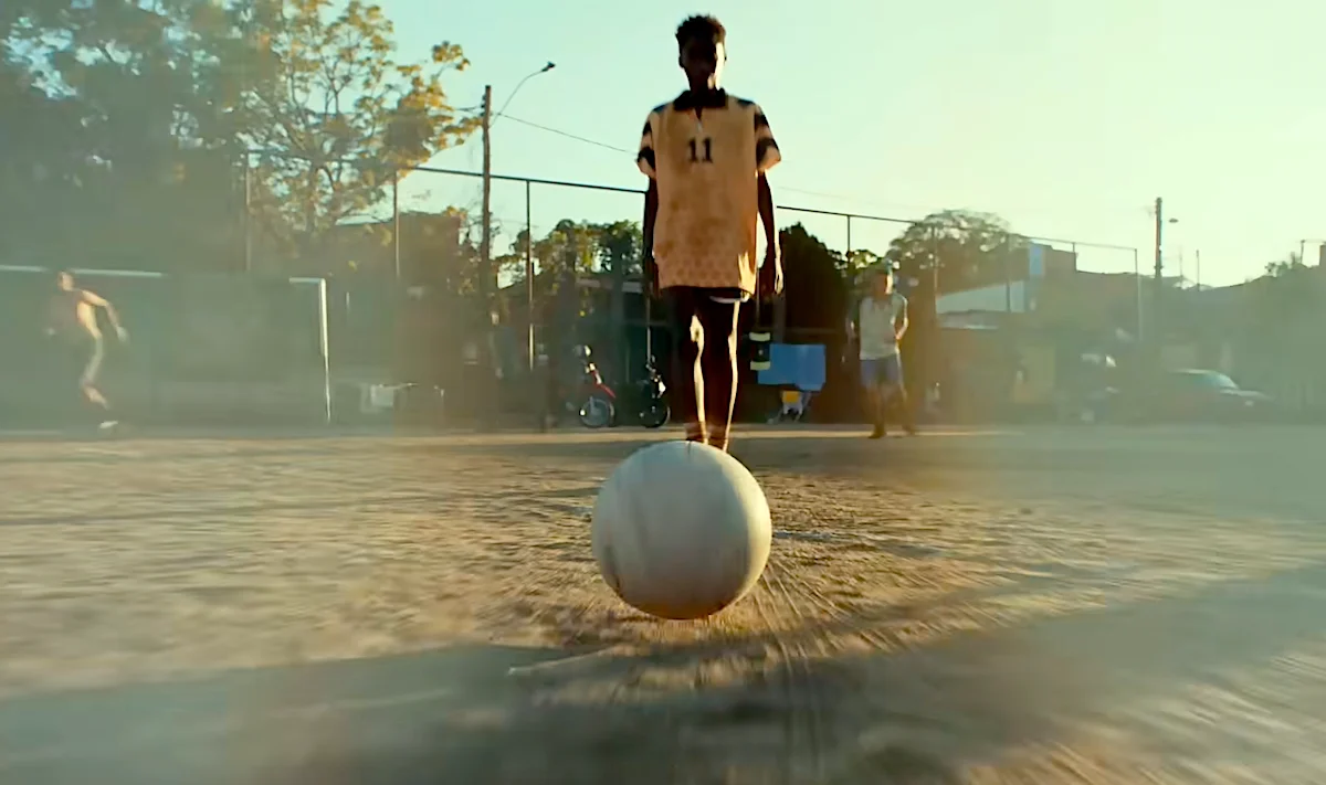 Mercado Livre celebra o futebol latino. Young soccer player standing with ball on urban field at sunset