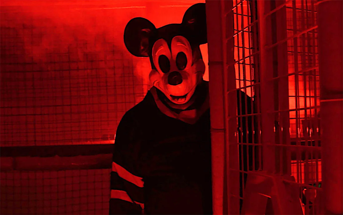Person in mouse costume in red lit room giving eerie vibe