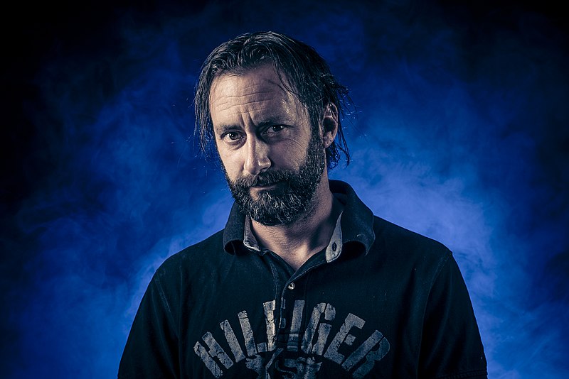 Bearded man with intense gaze in dramatic blue lighting and smoke background