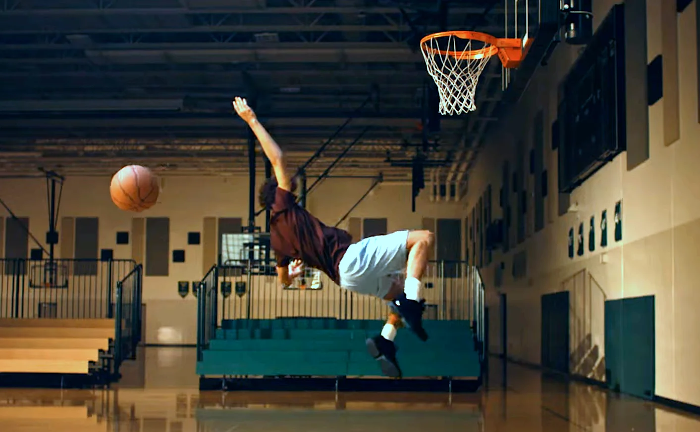 Basketball player performing an acrobatic dunk in an indoor gymnasium.