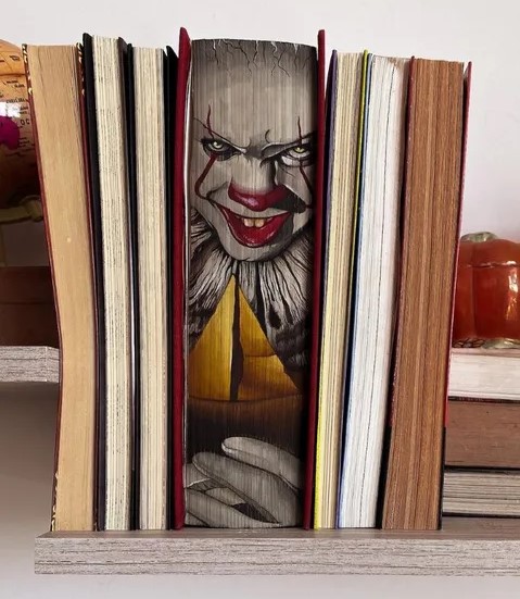 Artistic book edge painting of a clown face on a bookshelf.