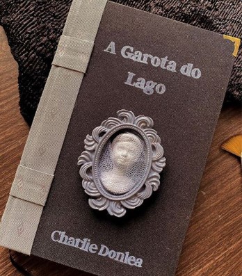 A Garota do Lago book by Charlie Donlea with ornamental cameo bookmark on textured surface.