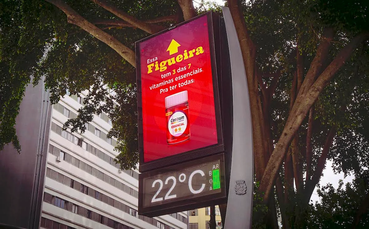 Digital billboard advertising Centrum vitamins with temperature display showing 22 degrees Celsius surrounded by trees in an urban setting