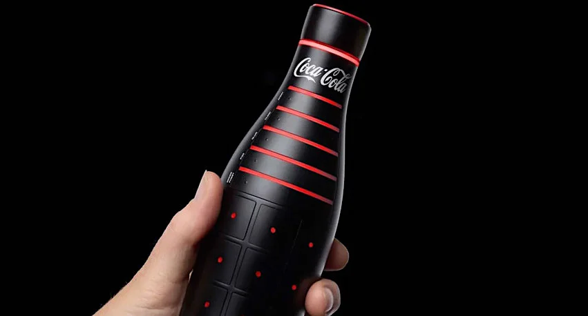 Hand holding limited edition black and red Coca-Cola bottle with sleek design against a black background.