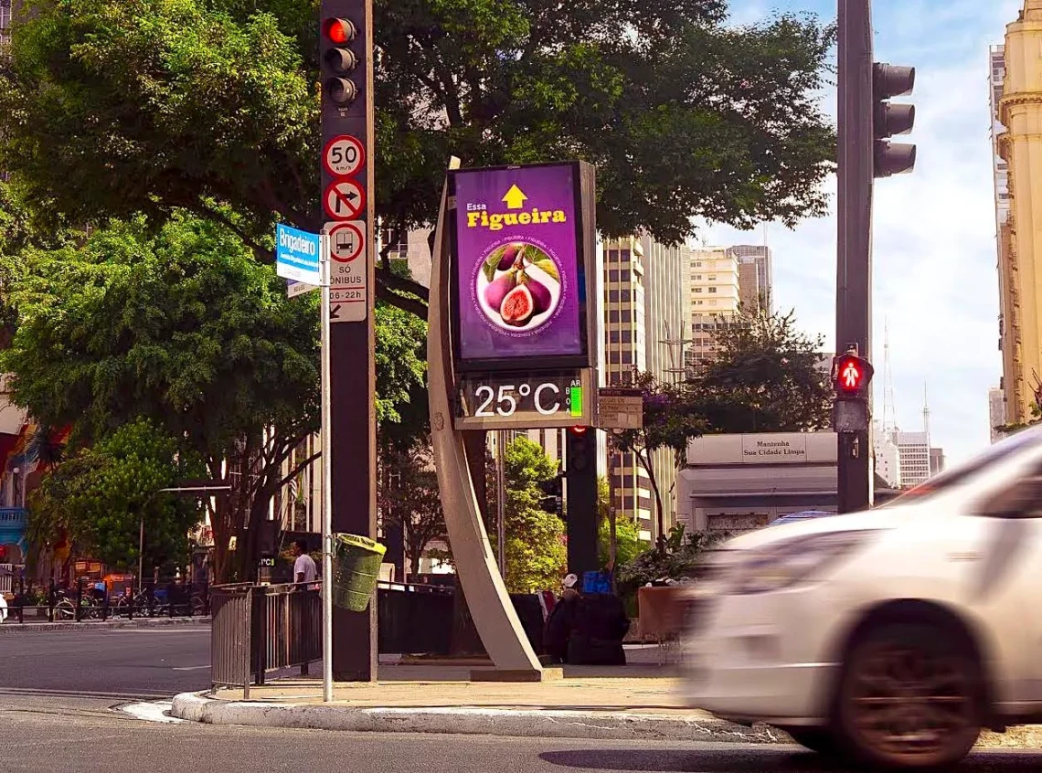 Geovitaminados. Digital billboard displaying advertisement and temperature at urban street intersection with traffic lights and moving car in city setting.