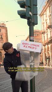 Young person attaching bubble wrap to a street pole with a sign reading Anti-Stress Remedy as a public stress relief initiative.