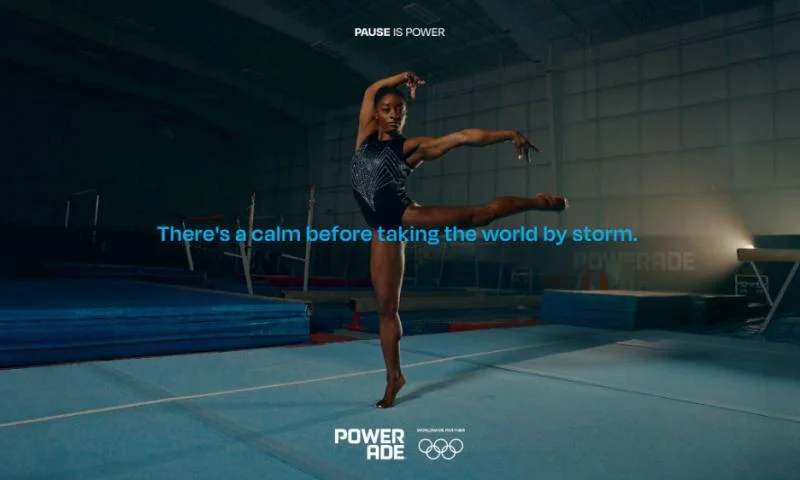 Pause is power. Female gymnast performing a balletic pose in a gym with Powerade branding and inspirational quotes