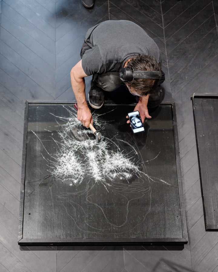 Top-down view of an artist creating a spark art piece with a hammer and an electronic device on a black canvas.