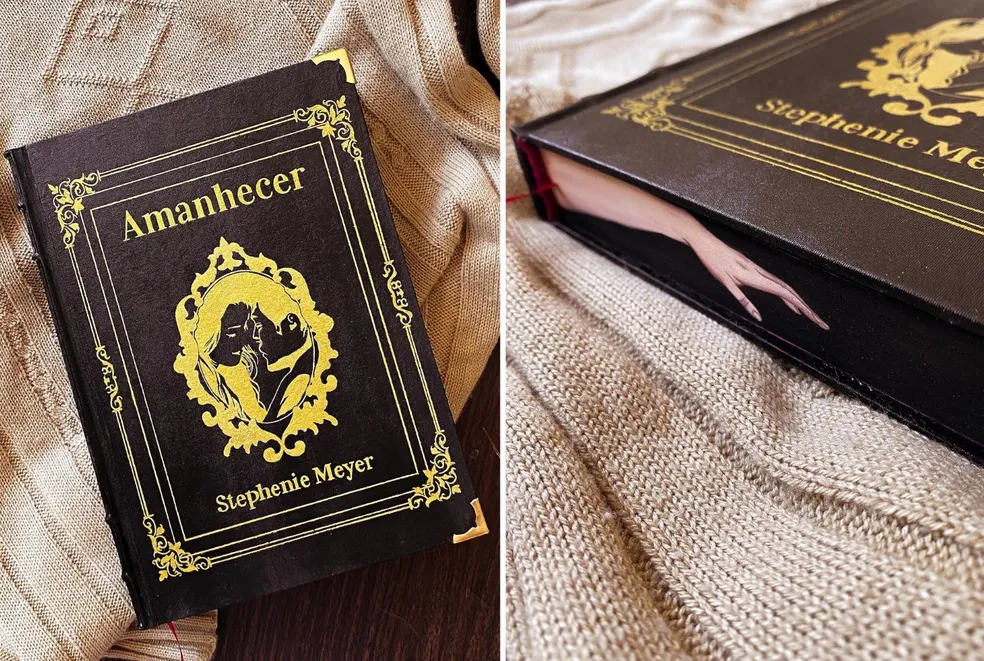 Stephanie Meyer's Amanhecer book cover with ornate gold detailing on a textured beige background, and a bookmark resembling a hand between pages.