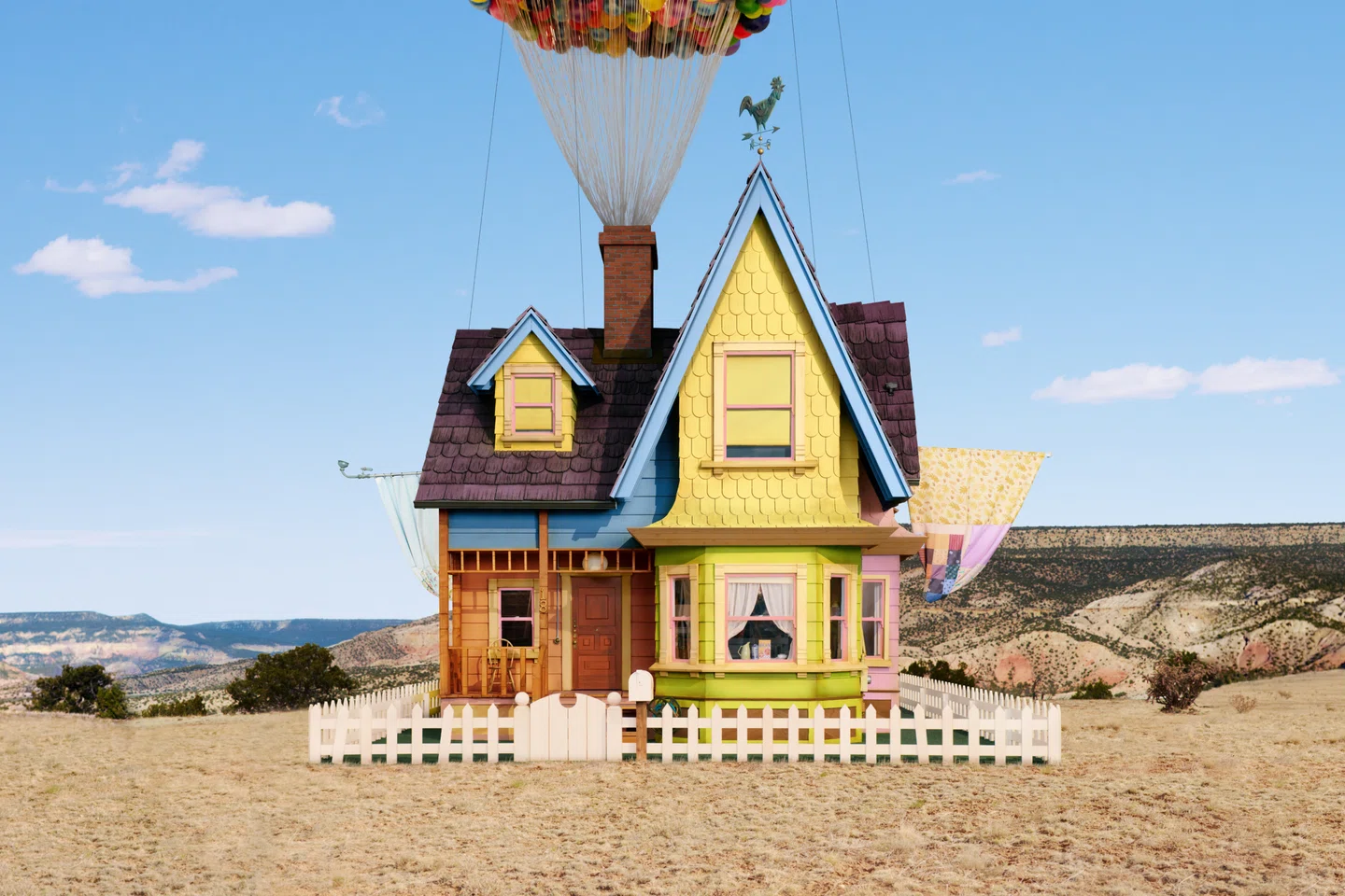 Colorful house lifted by balloons over desert landscape
