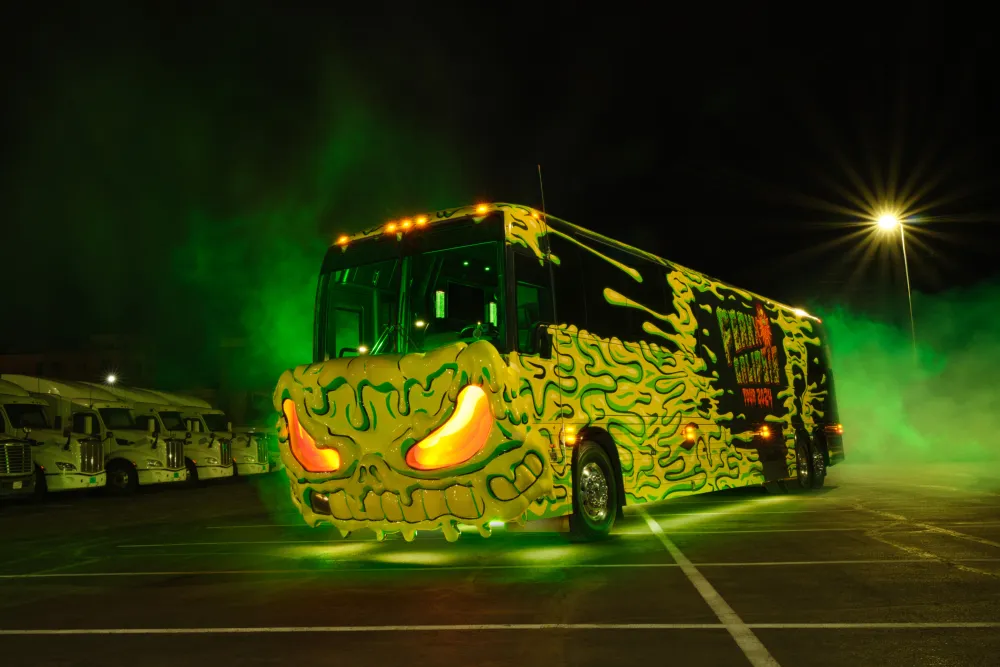 Customized bus with green flame designs and glowing eyes parked at night with a green smoke background.