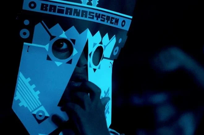 Person wearing a geometric mask with abstract patterns in blue lighting.