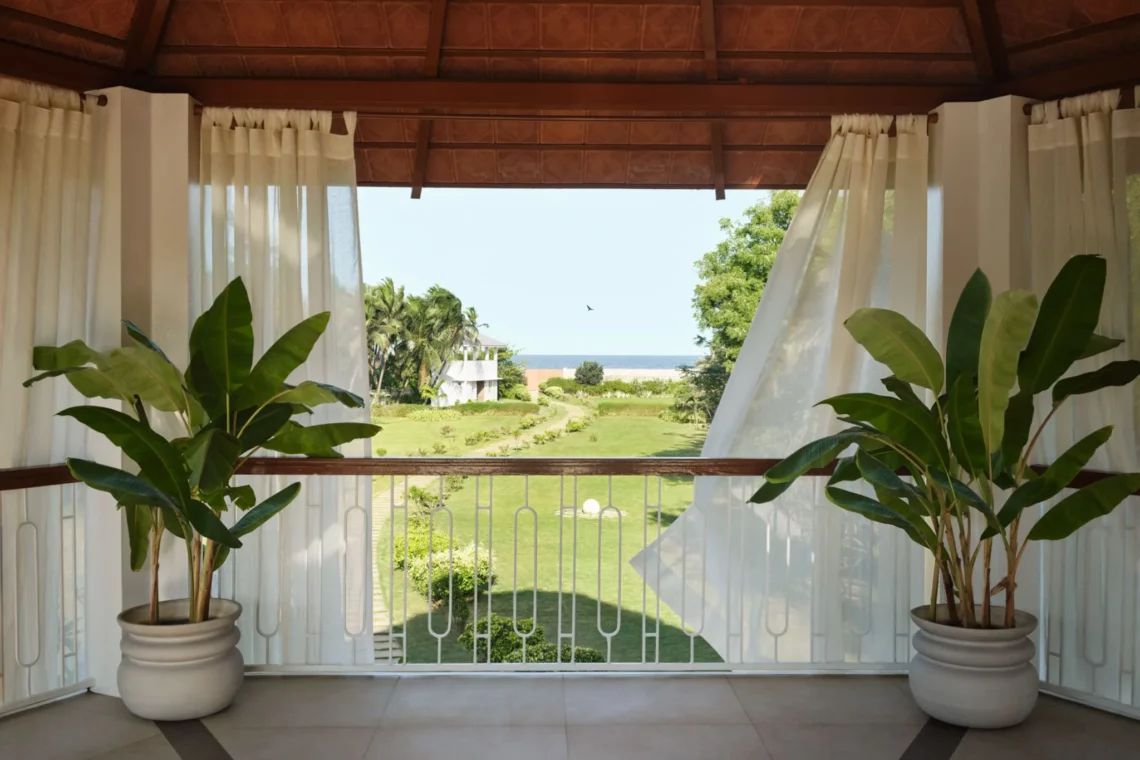 Ocean view from cozy balcony with white curtains and tropical plants in a serene resort setting.
