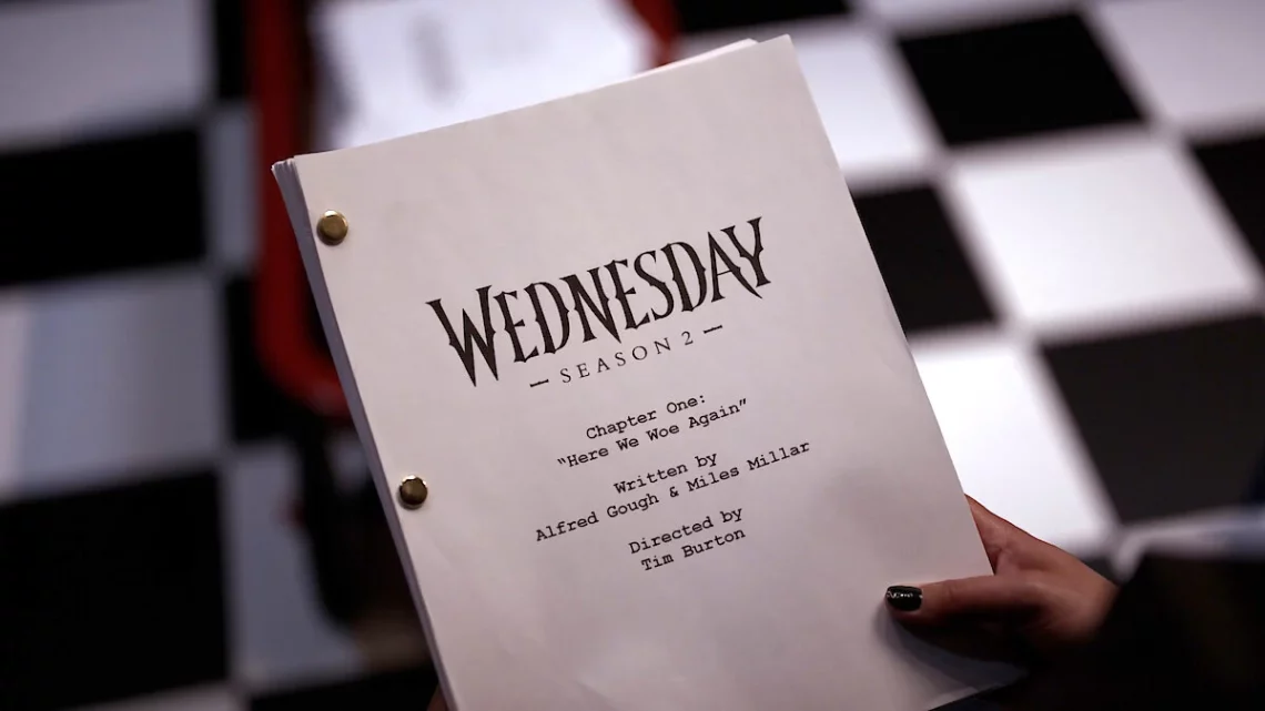 Wandinha Temporada 2. Hand holding Wednesday Season 2 script with title and credits on a checkered background