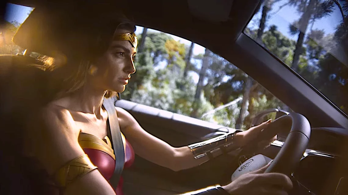 Woman in Wonder Woman costume driving a car with sunlight filtering through the trees.