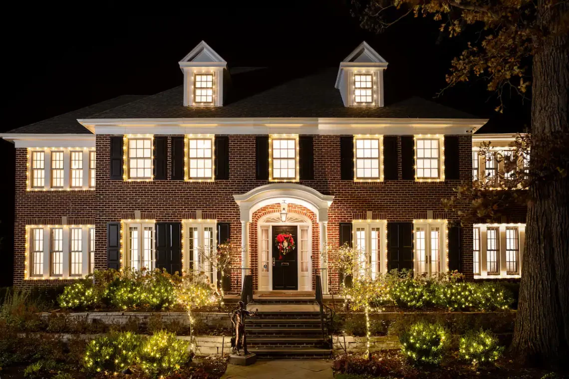 Elegant two-story brick house beautifully illuminated with warm exterior lighting and festive holiday decorations at night.